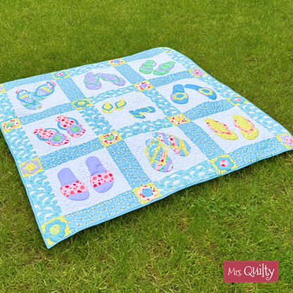 A playful blue and white Flip Flop Quilt, made from the downloadable PDF quilt pattern, is shown on green grass with creative quilting and a "Mrs. Quilty" label in the lower right corner.