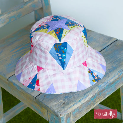 A Bucket Hat Downloadable PDF Quilt Pattern featuring pink and white gingham with colorful star and triangle patchwork sits on a distressed blue chair—ideal for beginners.