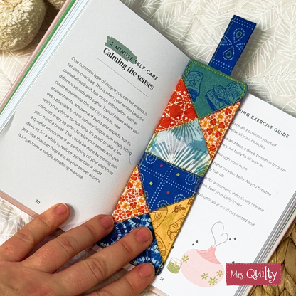 A hand holds open a book to a self-care page, featuring a colorful, quilted fabric bookmark made from our Bookmark Downloadable PDF Quilt Pattern—the perfect inspiration for your next instant digital craft project.