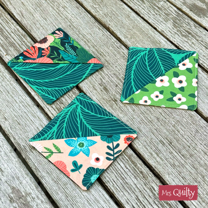 A set of three fabric coasters featuring floral and leaf patterns from quilting scraps is arranged on a rustic wooden surface. Each coaster showcases two contrasting designs. Product: Corner Bookmark Downloadable PDF Quilt Pattern.