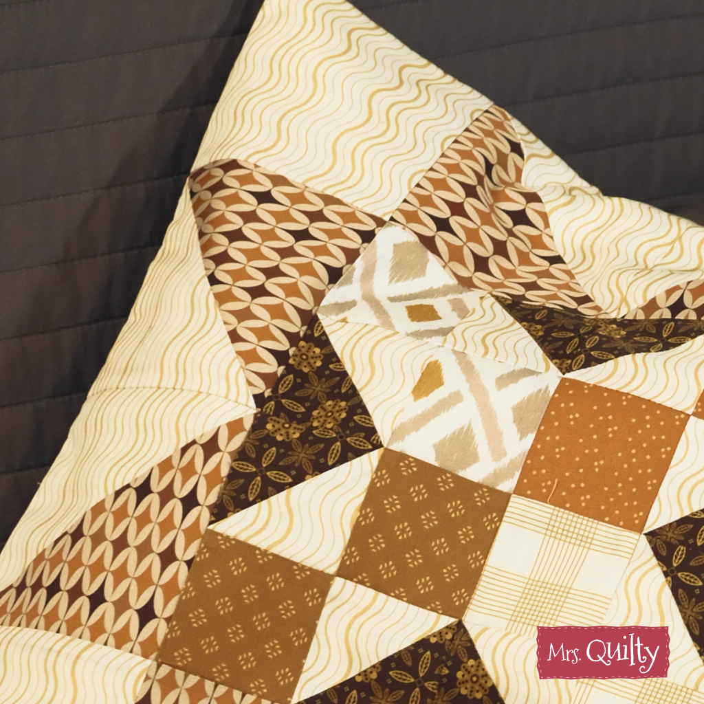 A close-up of a quilted pillow made using the Decorative Cushion Cover Downloadable PDF Quilt Pattern, featuring a geometric patchwork design in shades of brown and cream—ideal as decor or for quilting inspiration.