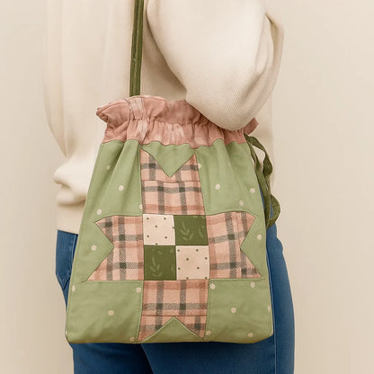 A person in blue jeans and a cream sweater carries a green and pink drawstring tote bag made using the Drawstring Tote Bag Quilt Downloadable PDF Quilt Pattern, featuring a patchwork star design.