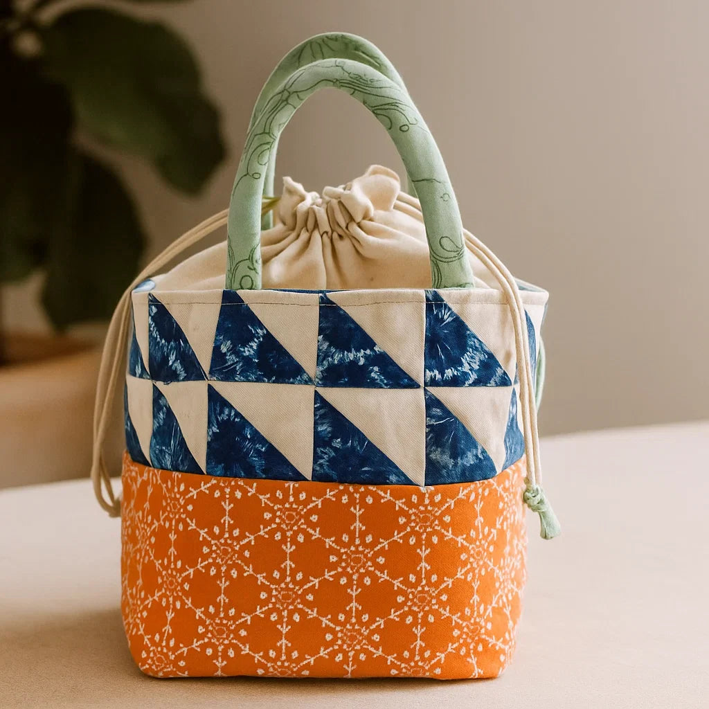 The Patch Pop Bucket Bag Quilt Downloadable PDF Quilt Pattern features blue and white triangle patchwork, orange patterned base, green handles, and a drawstring—perfect for intermediate quilters seeking an eye-catching project.