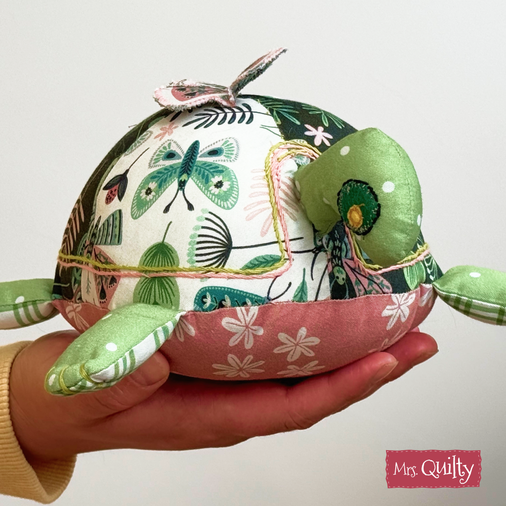 A hand holds a quilt made from the "Timmy the Turtle Downloadable PDF Quilt Pattern" featuring green, white, and pink fabrics—perfect for anyone who loves handmade gifts.